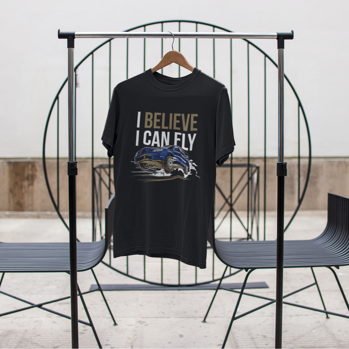 Black t-shirt with 'I Believe I Can Fly' text on a rack against a white wall.