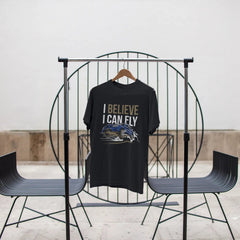 Black t-shirt with 'I Believe I Can Fly' text on a black metal stand against a white wall.