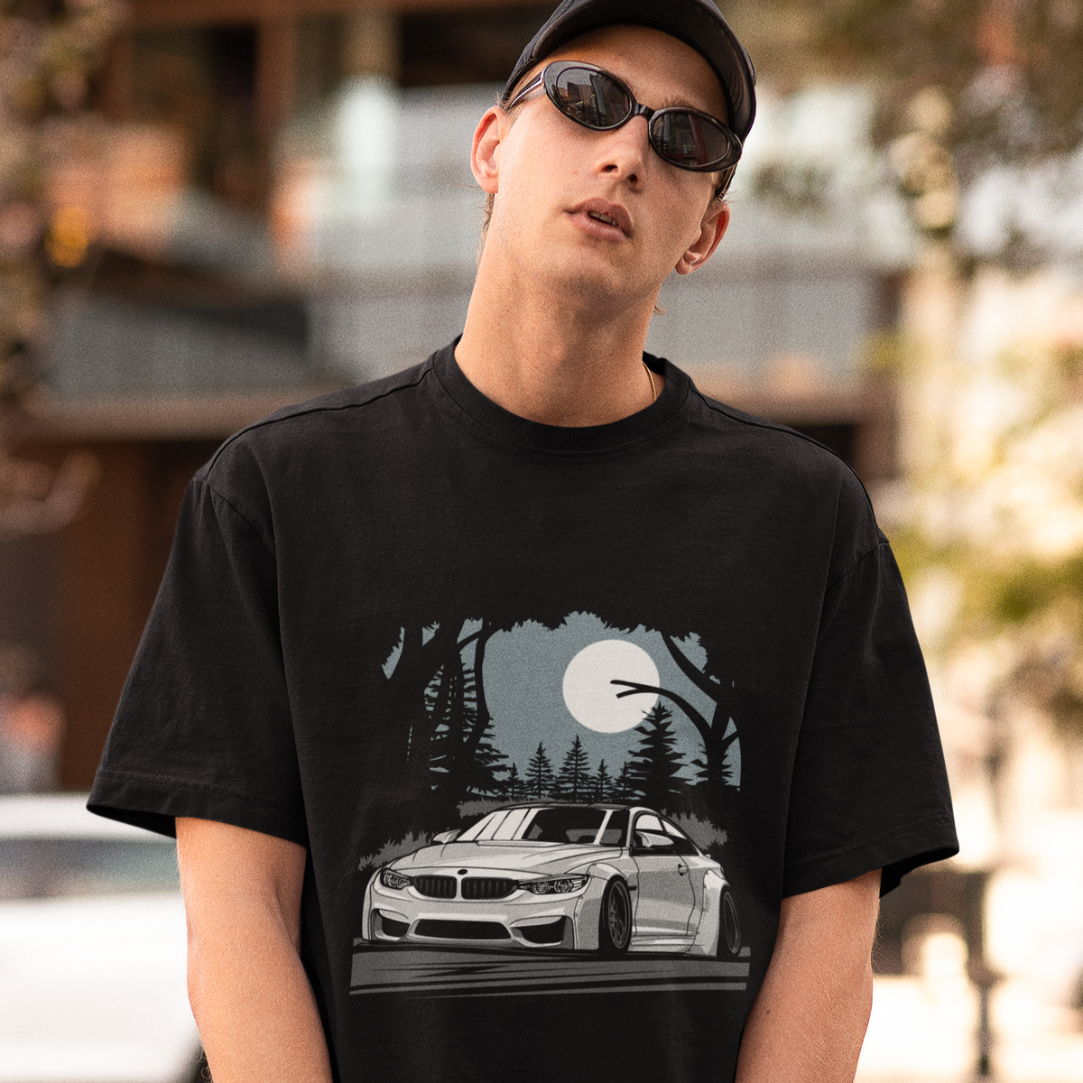 Person wearing a black t-shirt with a car graphic, standing outdoors.