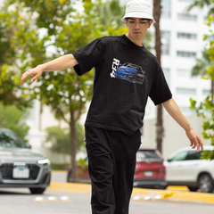 Person wearing a black t-shirt with a graphic design, black pants, and a white cap on a street.