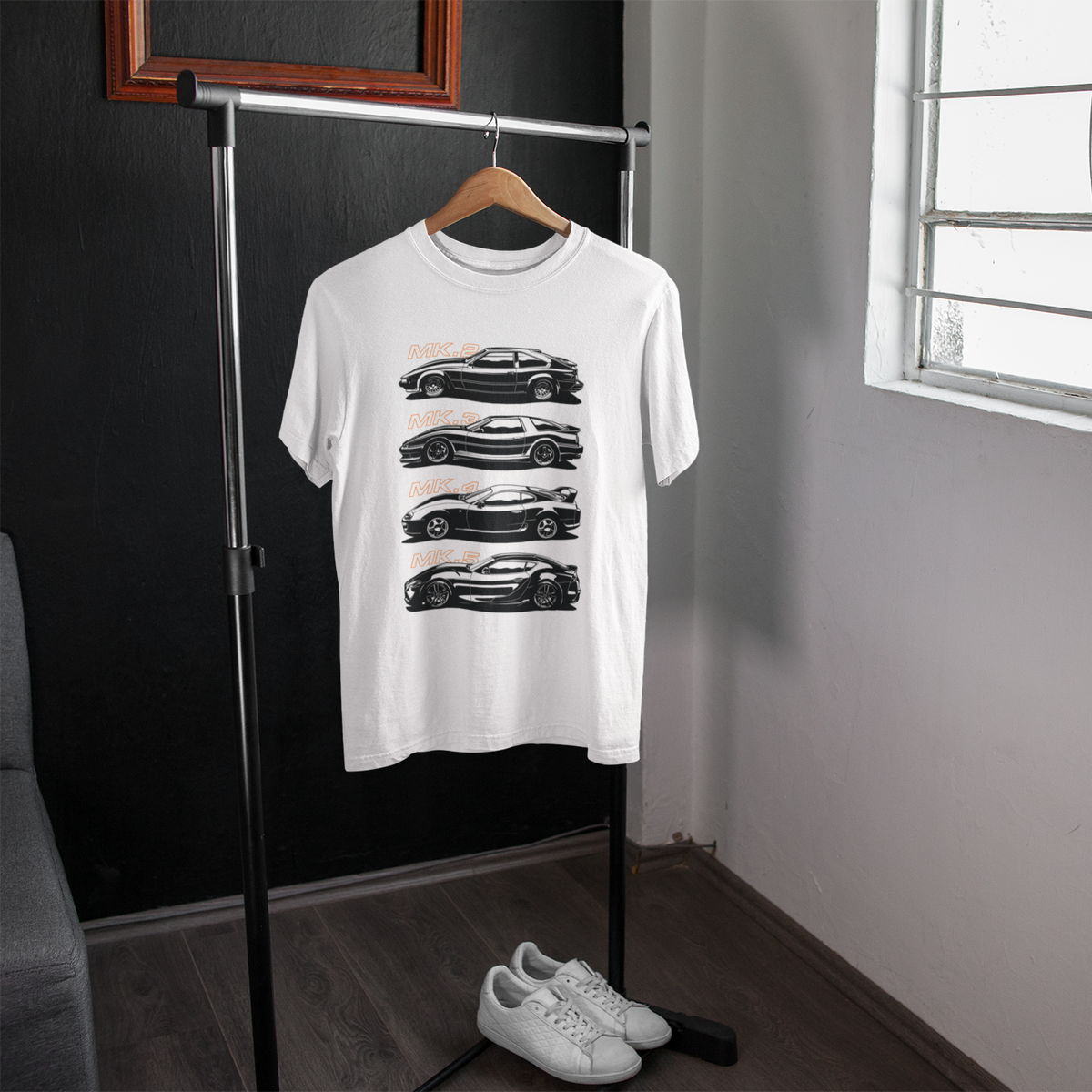 White t-shirt with black car graphics on a hanger in a room with a window.