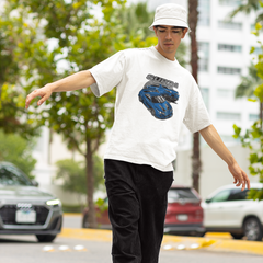 Person wearing a white t-shirt with a graphic design, black pants, and a white cap on a street.