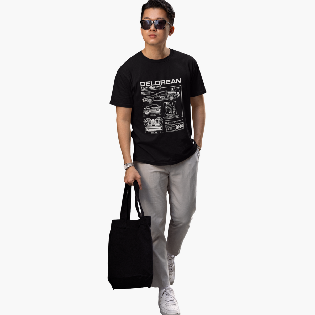 Person wearing a black t-shirt with 'Delorean' design, holding a black bag on a white background