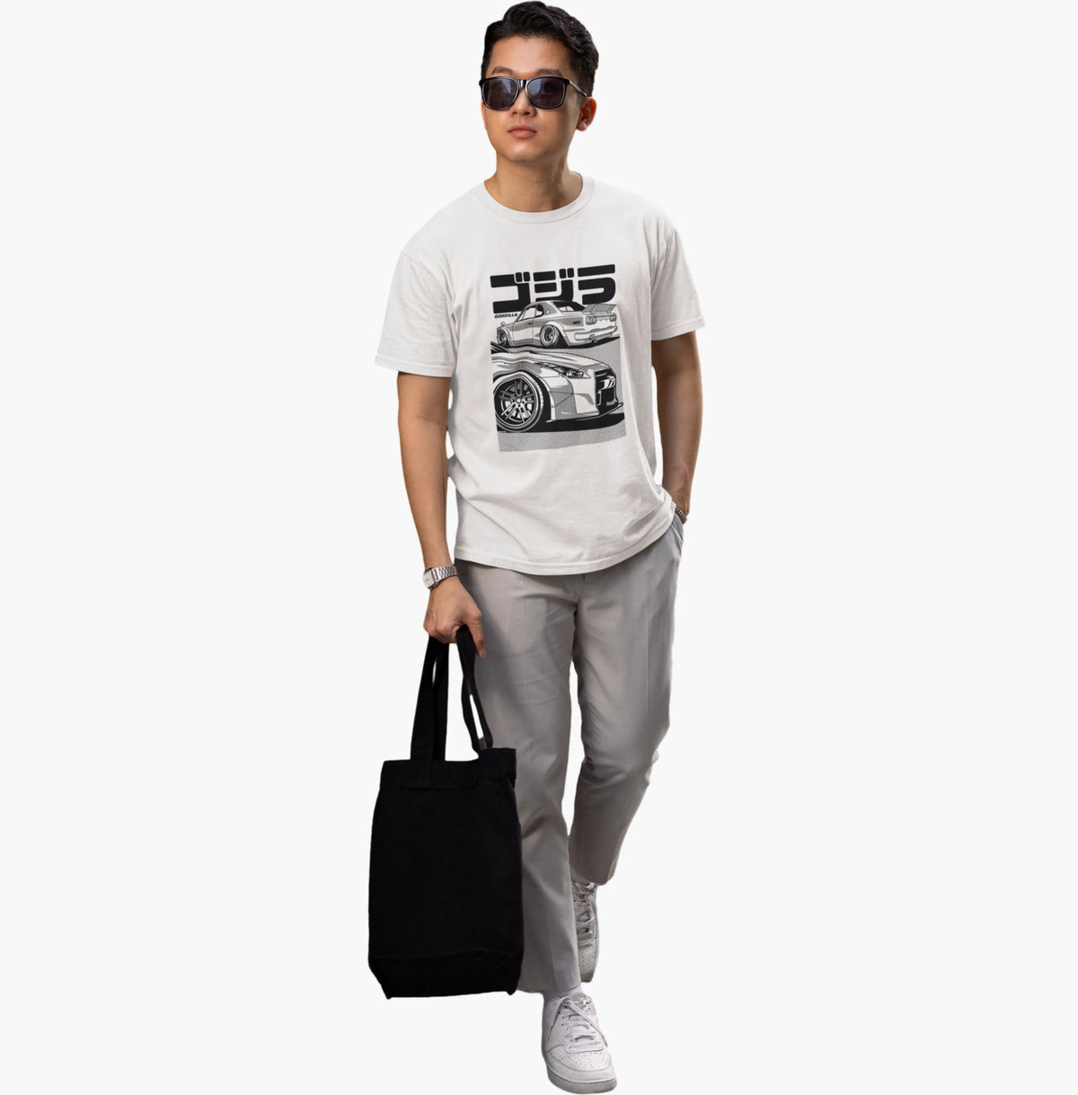 Person wearing a white t-shirt with a graphic design, holding a black tote bag on a white background