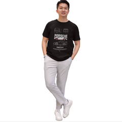 Man wearing a black t-shirt with Porsche logo and white pants on a white background