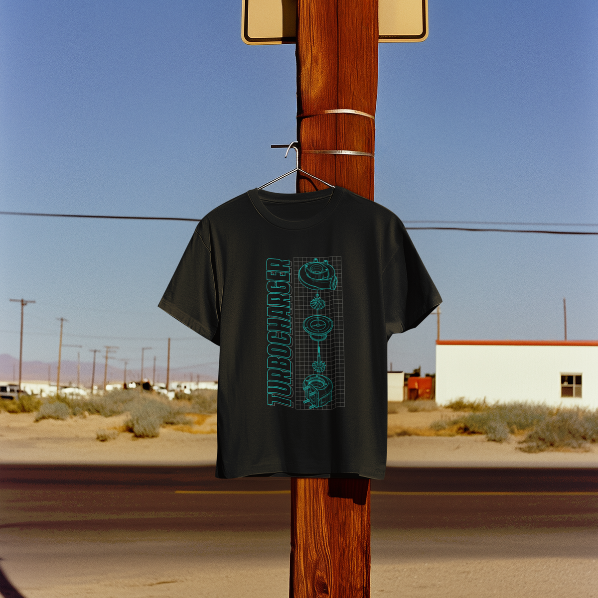 Black t-shirt with graphic design hanging on a wooden pole against a desert landscape.