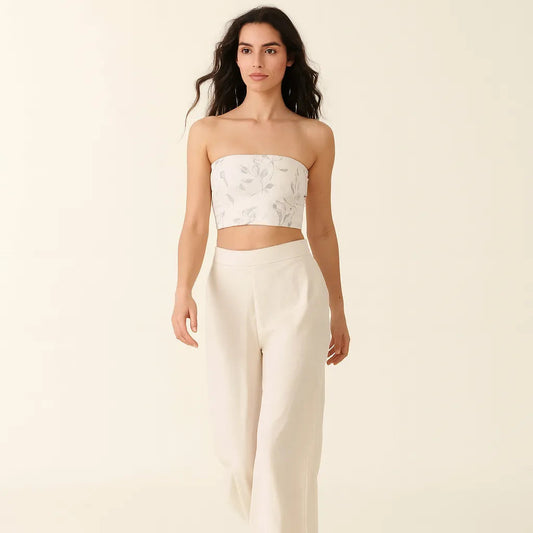 Woman wearing a white strapless top and pants on a beige background