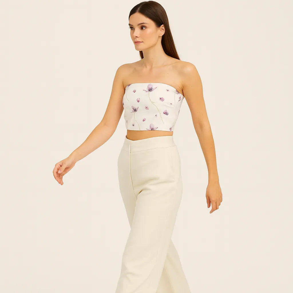Woman wearing a strapless floral top and white pants on a beige background