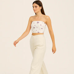 Woman wearing a strapless floral top and white pants on a beige background
