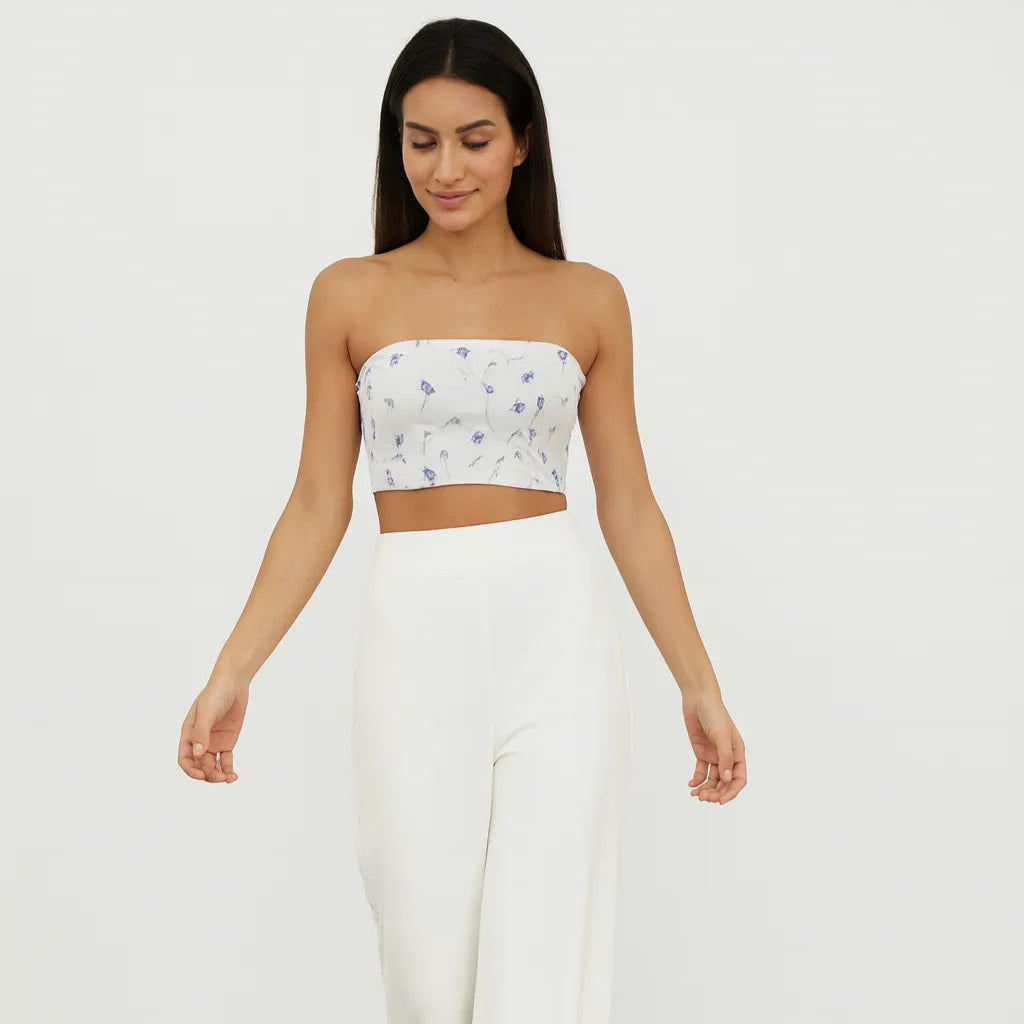 Woman wearing a strapless floral top and white wide-leg pants on a plain background