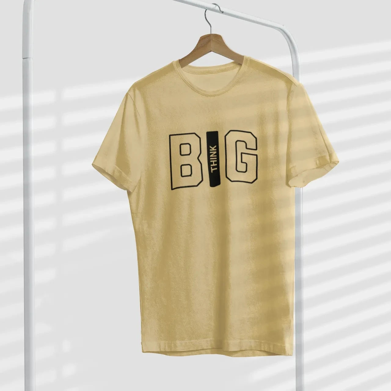 Beige t-shirt with 'BIG' printed on it hanging against a white background