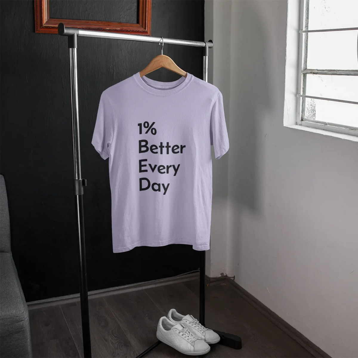 White t-shirt with '1% Better Every Day' text on a hanger in a room with a window.