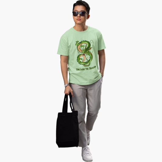 Person wearing a light green t-shirt with a graphic design, holding a black tote bag on a white background