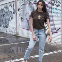 Woman standing in front of a graffiti-covered wall wearing a brown t-shirt, light blue jeans, and white sneakers.