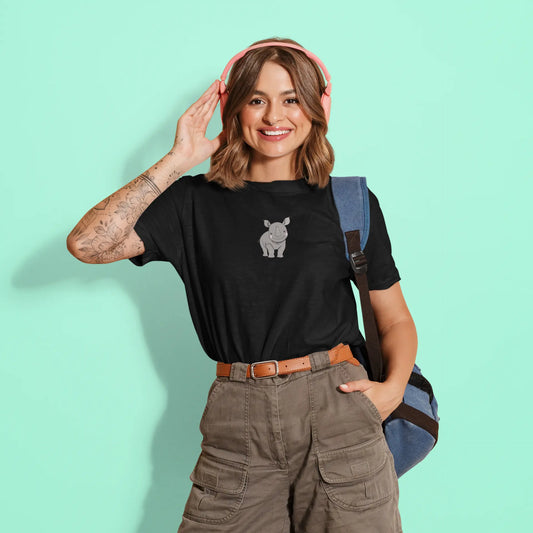 Woman wearing a black t-shirt with a graphic design, holding pink headphones, and standing against a light green background.