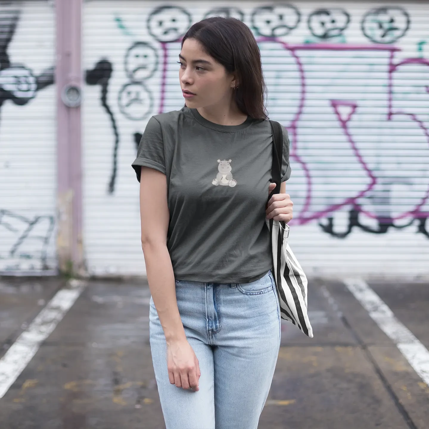 Woman wearing a gray t-shirt with a bear graphic and light blue jeans, standing in front of a graffiti-covered wall.