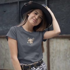Woman wearing a dark gray t-shirt with a skull design and a black hat, standing against a textured wall.