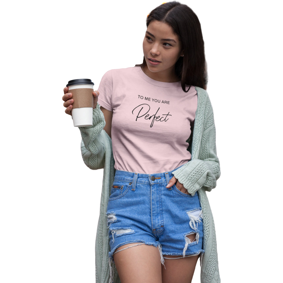 Woman wearing a pink t-shirt with text, holding a coffee cup, and wearing a light green cardigan and blue shorts on a white background.