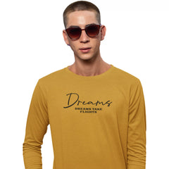 Man wearing a mustard yellow long-sleeve shirt with text, standing against a white background