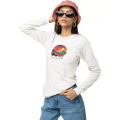 Person wearing a white long-sleeve shirt with a colorful graphic and text, blue jeans, pink hat, and sunglasses on a white background.