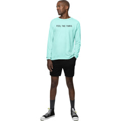 Man wearing a light blue long-sleeve shirt with 'FEEL THE THRIL' text, black shorts, and black sneakers on a white background.
