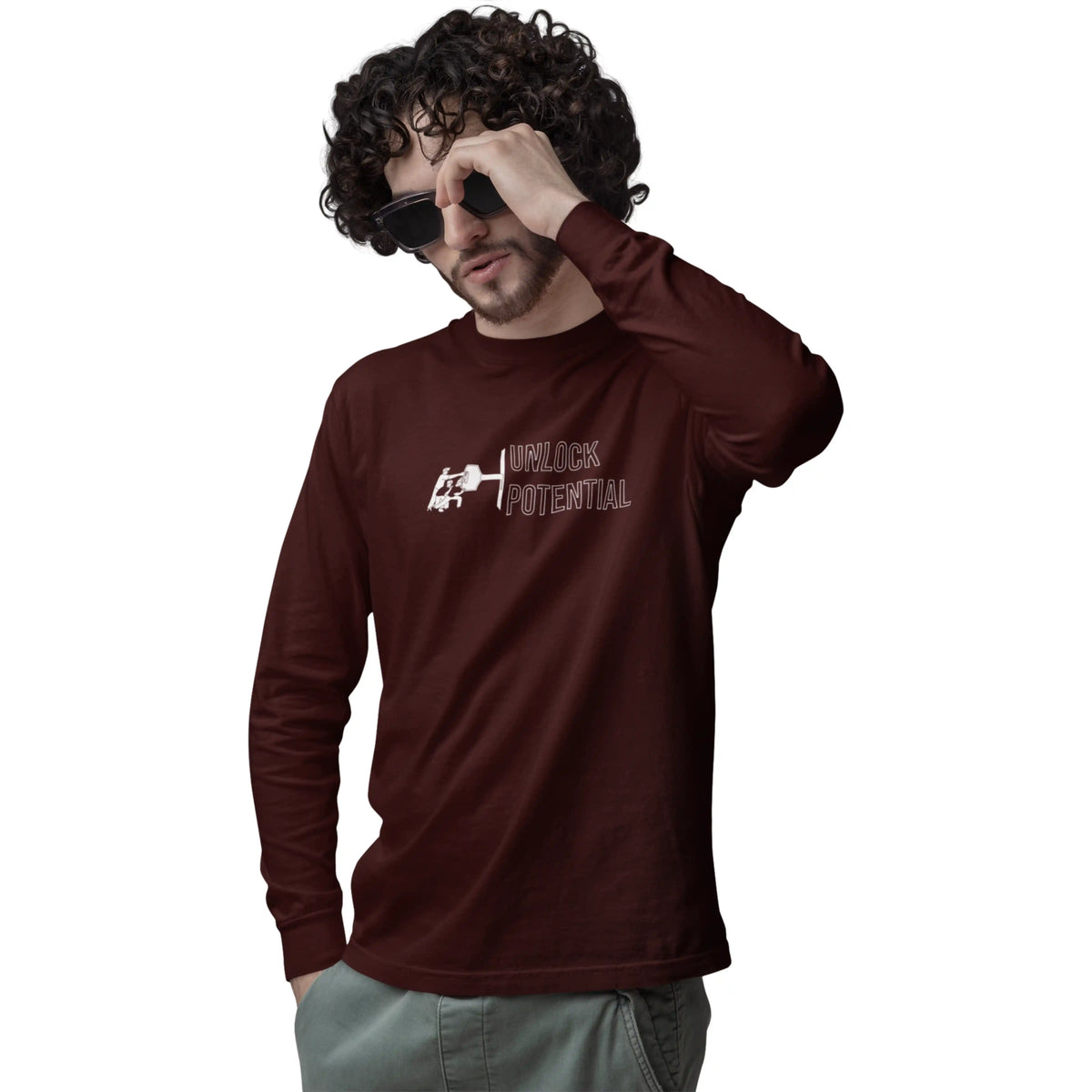 Man wearing a brown long-sleeve shirt with a logo and text, holding sunglasses to his face on a white background.
