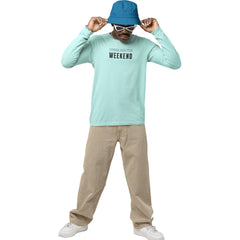 Person wearing a light blue long-sleeve shirt with text, beige pants, and a blue bucket hat on a white background