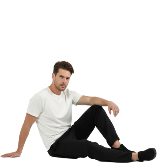 Man sitting on the floor wearing a white t-shirt and black pants against a white background